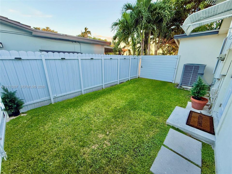 Fenced backyard featuring a manicured lawn, privacy fencing, concrete pavers, and mature palms