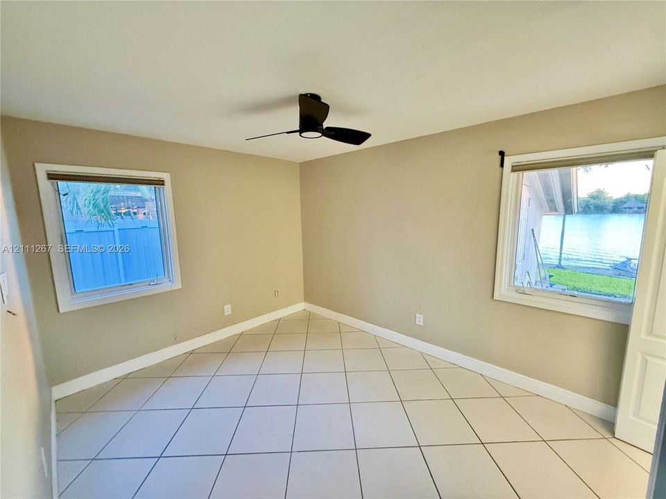 Interior space featuring ceramic tile flooring, neutral wall paint, two windows with blinds, and a ceiling-mounted light fixture with fan blades