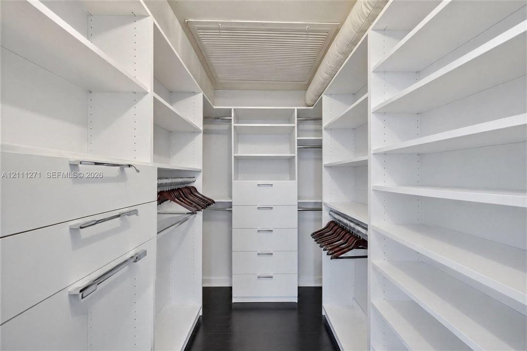 Walk-in closet featuring extensive built-in white shelving, multiple storage drawers with silver-tone hardware, and wood-finish flooring