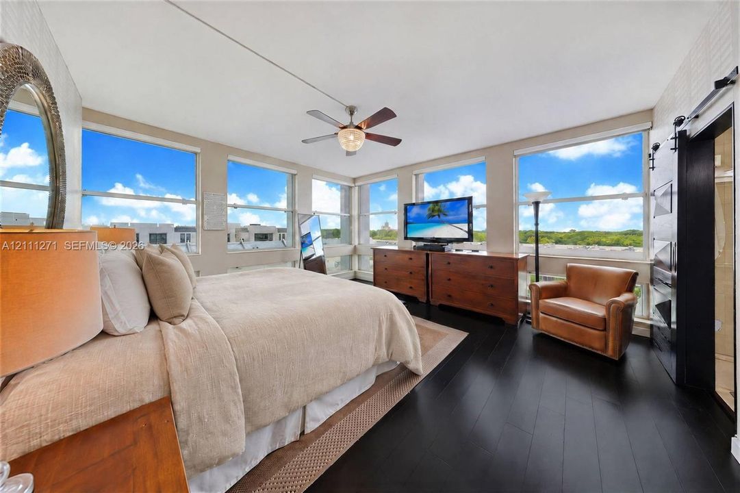 Expansive floor-to-ceiling windows, dark wood-finish flooring, ceiling fan with integrated lighting, and black sliding barn door