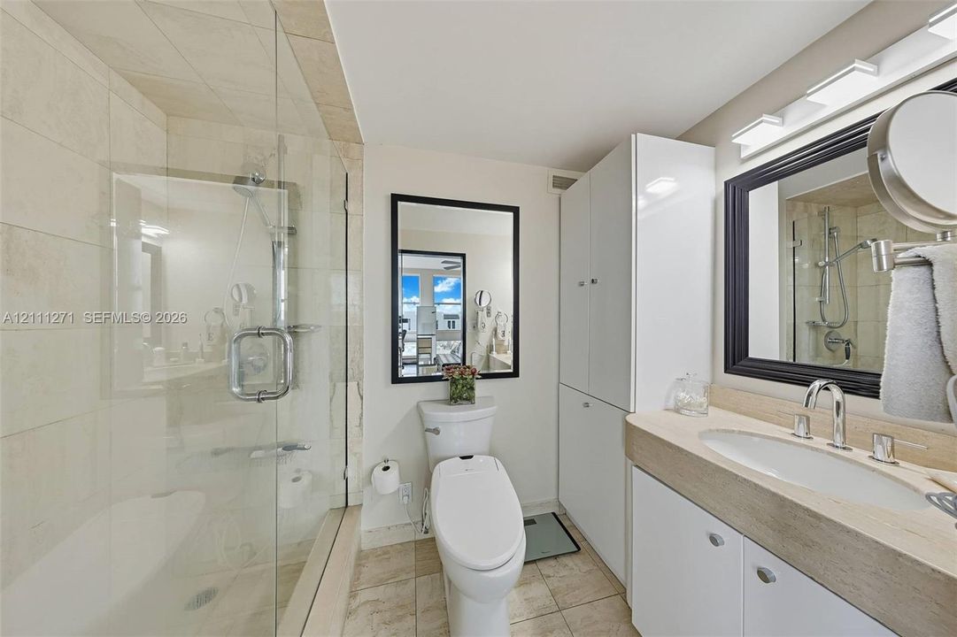 Bathroom featuring a walk-in shower with glass enclosure, tile surround, stone-top vanity with undermount sink, built-in floor-to-ceiling cabinetry, and ceramic tile flooring