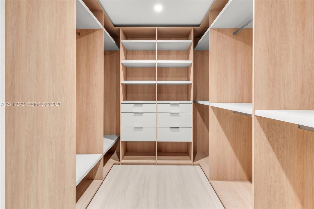Custom walk-in closet featuring floor-to-ceiling wood-finish cabinetry, built-in shelving, integrated hanging rods, and stacked drawer storage with clean-lined hardware