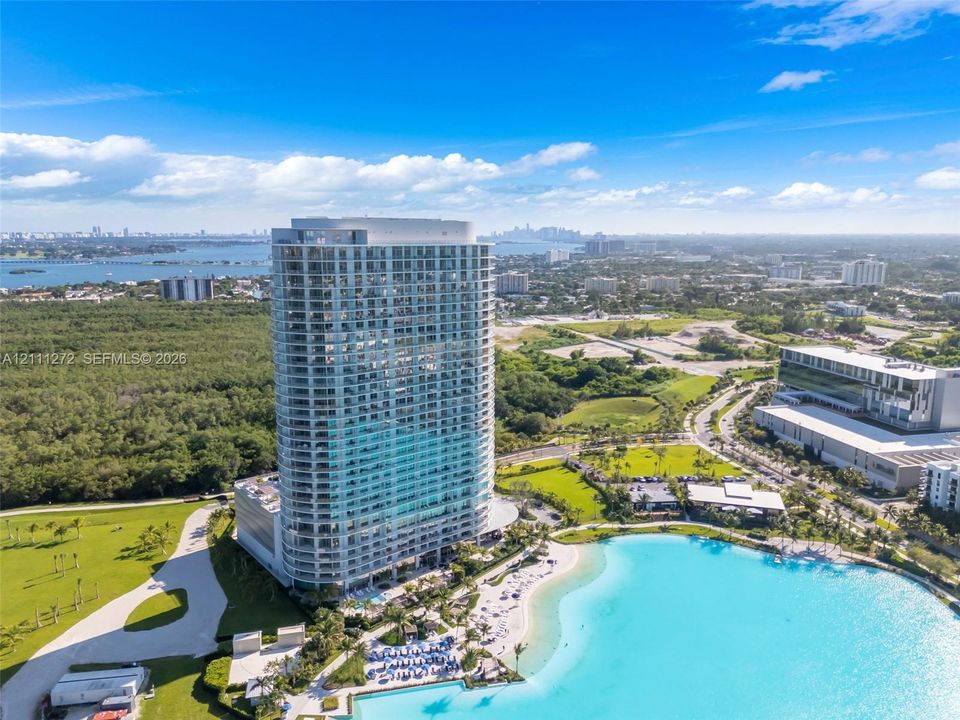 High-rise residential tower featuring a glass facade, expansive balconies, ground-level swimming pool, and an integrated recreational water feature
