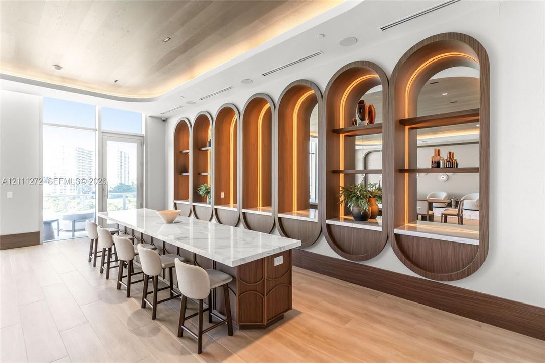 Extended island featuring a stone-style countertop, integrated arch-framed shelving with recessed lighting, mirrored backings, wood-finish flooring, and a curved ceiling soffit