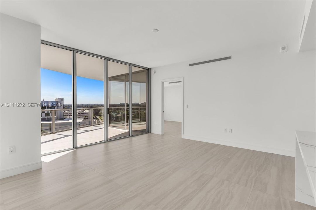 Open-concept interior featuring floor-to-ceiling sliding glass doors, a covered balcony, large-format tile flooring, and a stone-surface counter