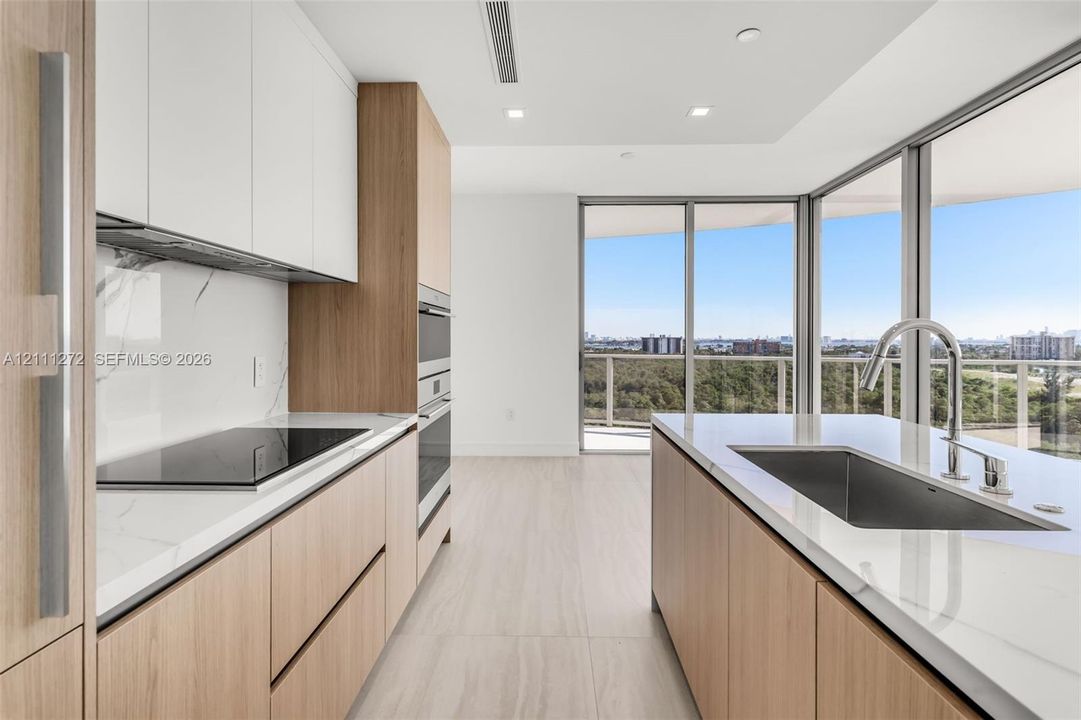 Kitchen featuring wood-finish flat-panel cabinetry, white stone countertops, matching full-height backsplash, built-in stainless steel appliances, and a kitchen island with an undermount sink