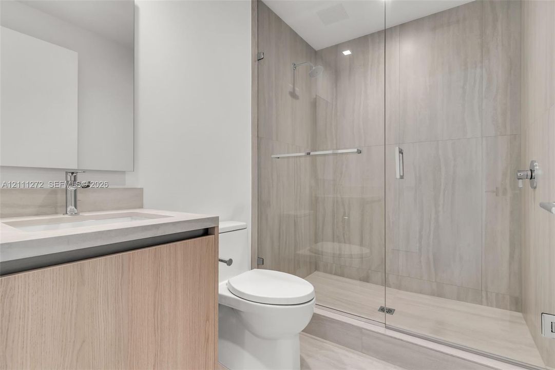 Bathroom featuring a wood-finish vanity with a stone countertop, an integrated sink, polished chrome plumbing fixtures, and a glass-enclosed shower with large-format tile surround