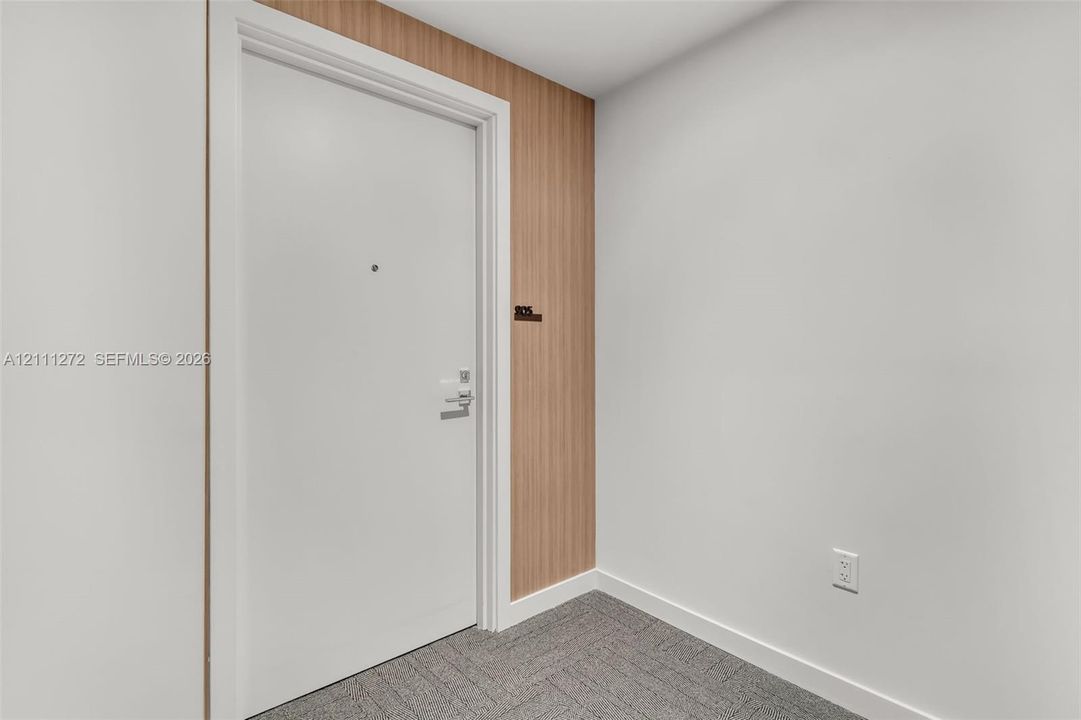 Entryway featuring a solid door with integrated peephole and metal hardware, accent wall with vertical wood-finish paneling, and neutral carpeting
