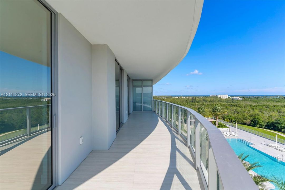 Curved balcony featuring light-toned tile flooring, floor-to-ceiling glass sliding doors, and a glass-paneled railing