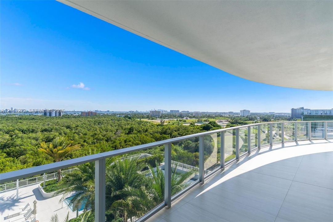 Curved balcony featuring large-format tile flooring and a glass-paneled metal railing overlooking expansive natural landscape and urban surroundings