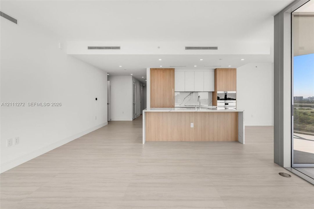 Kitchen featuring two-tone wood-finish and white cabinetry, stone-finish backsplash, built-in stainless steel appliances, and a central island with a stone-finish countertop, finished with light-toned wood-finish flooring and recessed lighting
