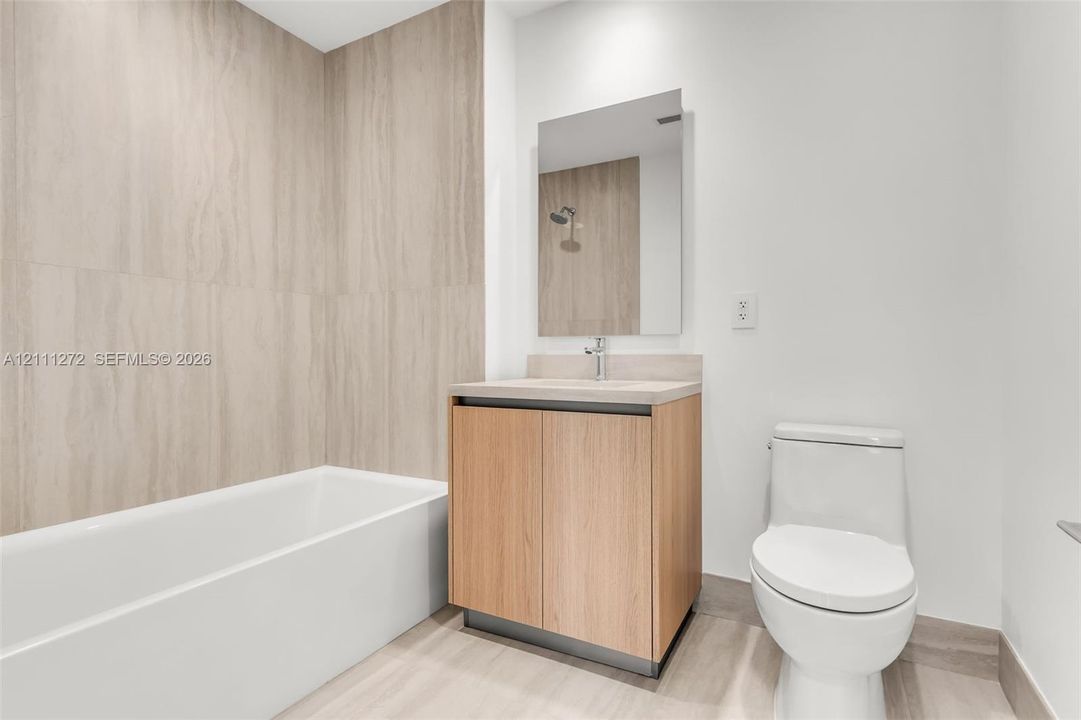 Bathroom featuring floor-to-ceiling textured tile surround, built-in vanity with wood-finish cabinetry, countertop basin, rectangular wall-mounted mirror, and wood-finish flooring