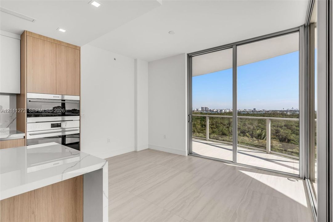 Floor-to-ceiling sliding glass doors opening to a private balcony, wood-finish cabinetry, built-in stainless steel wall ovens, and stone-surfaced island countertop