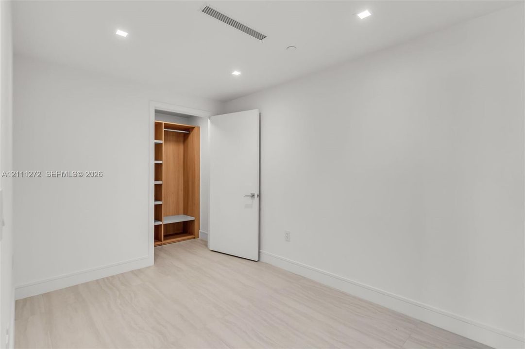 Minimalist room featuring light wood-finish flooring, recessed ceiling lighting, a flush-mount interior door, and a built-in closet with integrated shelving