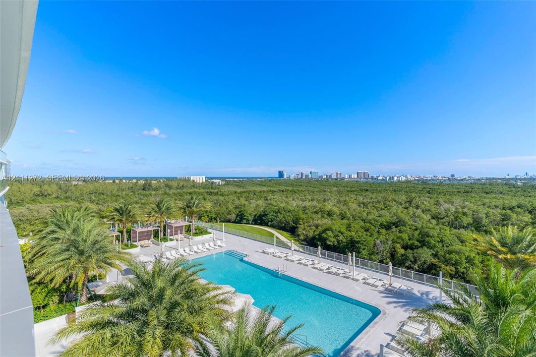 Swimming pool featuring a paved deck, perimeter fencing, palm tree landscaping, and coastal cityscape backdrop