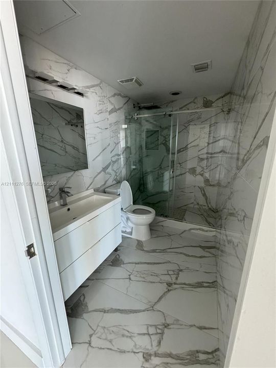 Bathroom featuring large-format veined tile flooring and wall surfacing, a wall-mounted floating vanity with integrated sink, and a glass-enclosed shower with polished metal hardware