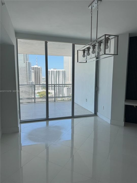 Floor-to-ceiling glass panels, expansive covered balcony, polished tile flooring, and geometric metal-frame chandelier