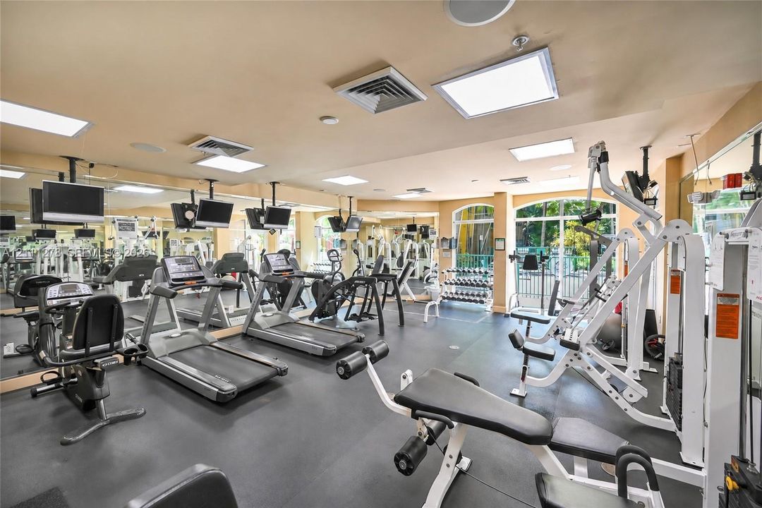 Fitness center featuring wall-to-wall mirrors, recessed lighting, rubberized flooring, and expansive arched windows