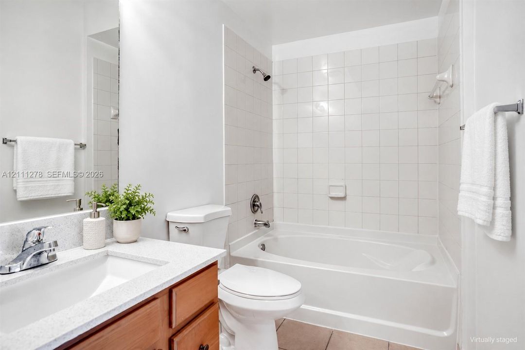Bathroom featuring a wood-finish vanity with a stone-composite countertop, integrated sink, chrome-finished hardware, and a tub-shower combination with white ceramic wall tile
