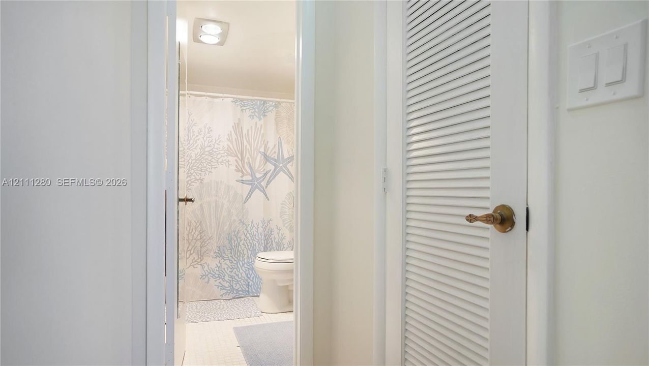 White louvered door featuring brass hardware, square-edged white door casing, and white light switch plate