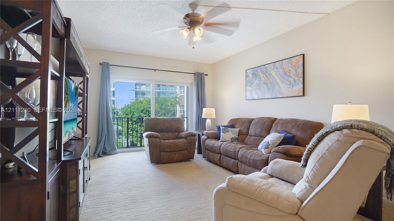 Living area featuring sliding glass doors, a ceiling fan with integrated lighting, and a metal-railing balcony