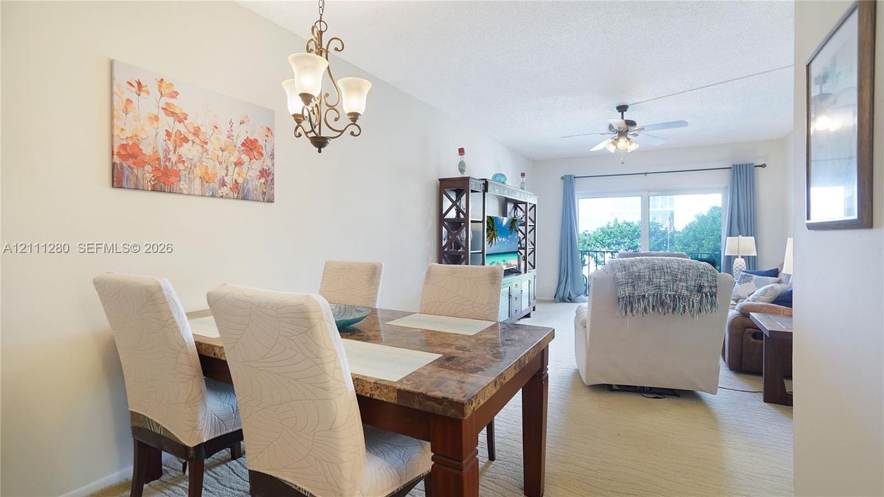 Open-concept interior featuring vaulted ceilings, a decorative wrought-iron chandelier, ceiling fan with integrated lighting, and sliding glass doors