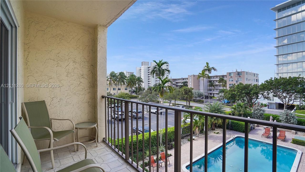 Covered balcony featuring tile flooring and metal railings, overlooking an in-ground swimming pool and landscaped grounds
