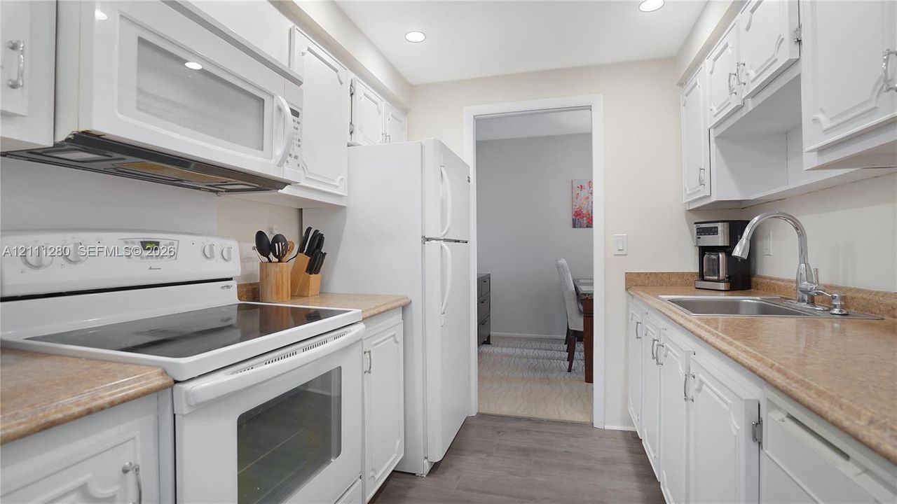 Kitchen featuring white cabinetry, solid-surface countertops, recessed lighting, and white appliances