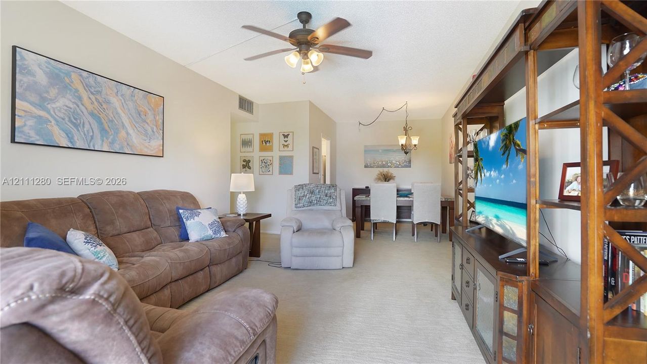 Living area featuring neutral carpeting, a ceiling fan with integrated lighting, and a multi-arm overhead chandelier