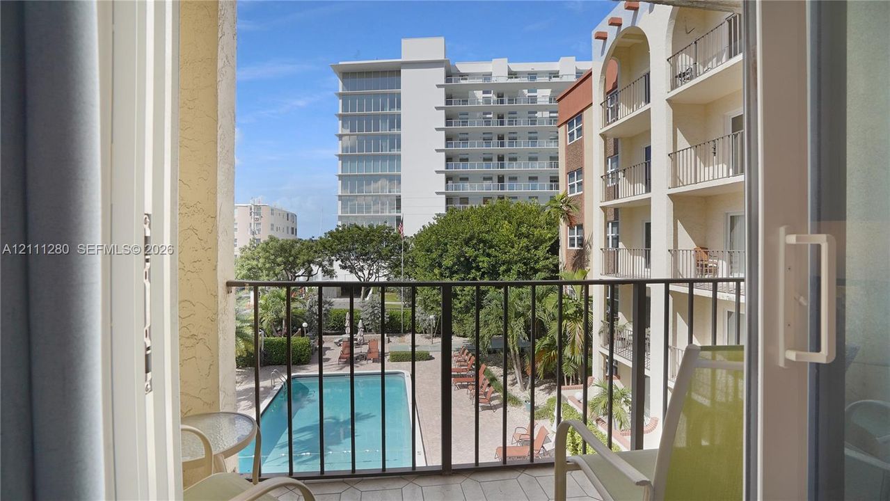 Balcony with metal railing overlooking an in-ground swimming pool and landscaped grounds