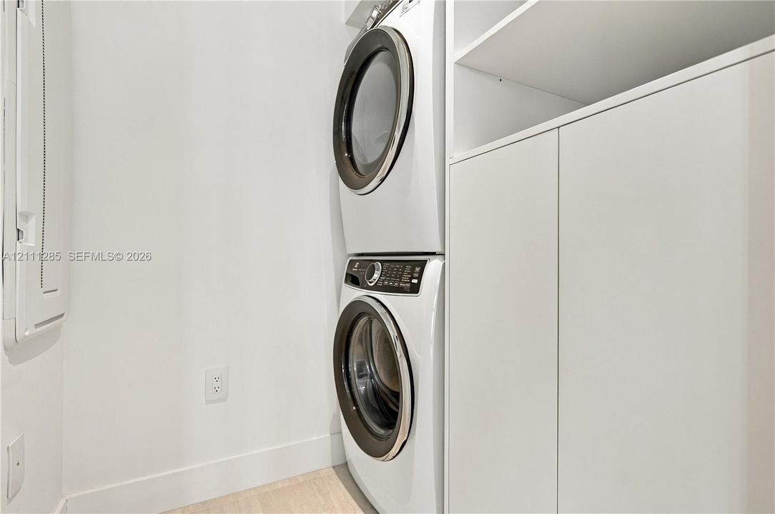 Laundry area featuring a stackable front-load washer and dryer, integrated white cabinetry with open shelving, and light-toned flooring