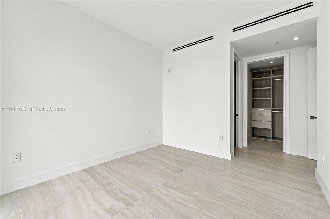 Neutral-toned tile flooring, built-in wooden closet system with shelving and drawers, and recessed linear ceiling detailing