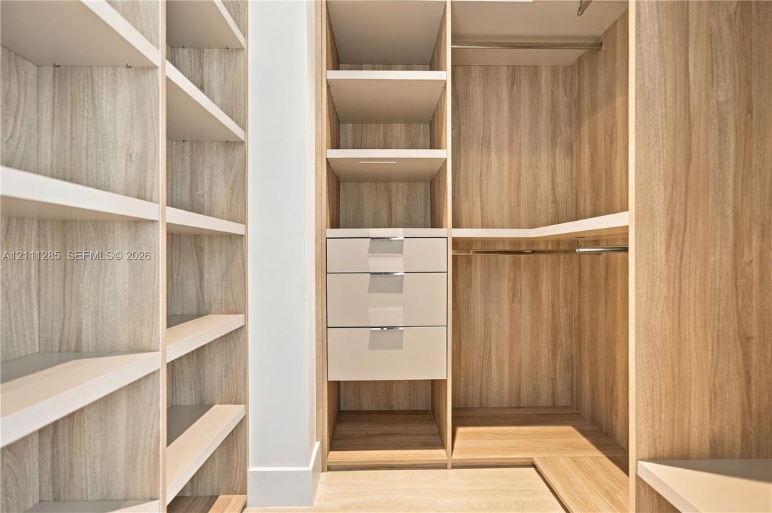 Custom walk-in closet featuring wood-finish cabinetry, built-in shelving, integrated drawers with metal pulls, and polished metal hanging rods