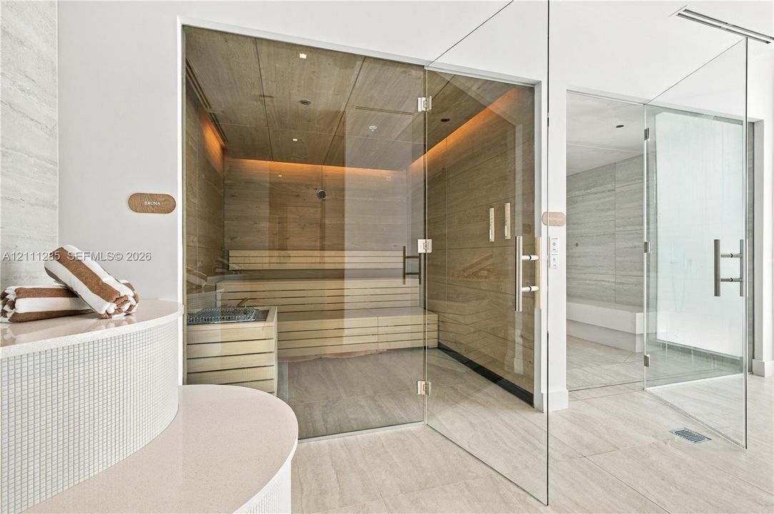 Custom sauna featuring wood-panelled interior, multi-level bench seating, and glass enclosure, paired with a glass-enclosed steam shower featuring neutral-toned wall tiles and tile flooring