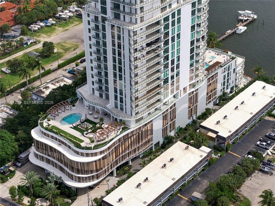 High-rise residential tower featuring a multi-level structure, wraparound balconies, an elevated swimming pool with a sprawling sun deck, and integrated waterfront access