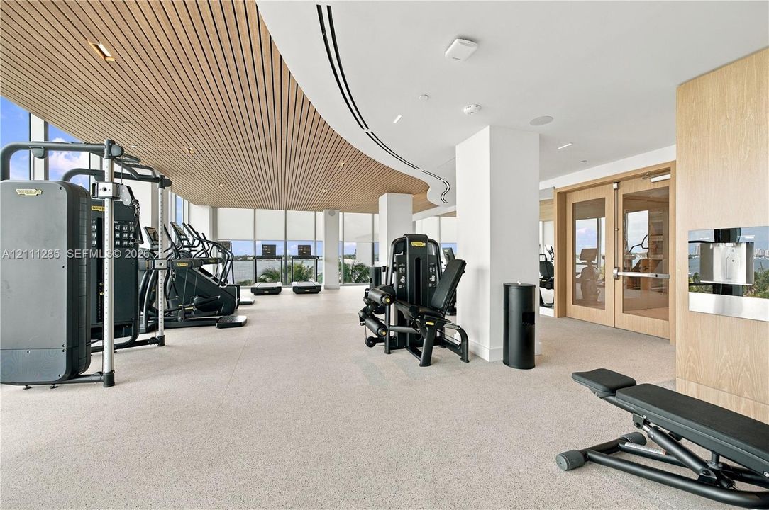 Fitness center featuring floor-to-ceiling windows, slatted wood-finish ceiling, recessed lighting, and wall-mounted water dispenser