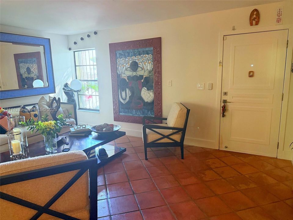 Terracotta tile flooring, multi-pane window with security bars, and solid-core paneled entry door
