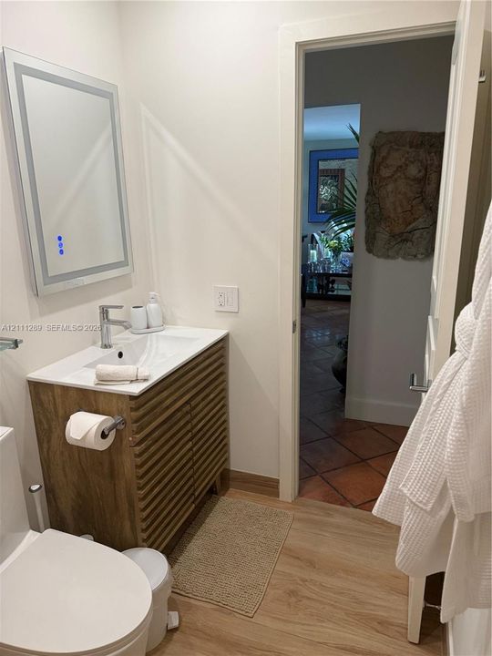 Slatted wood-finish vanity with integrated sink, rectangular white countertop, sleek metal faucet, and wall-mounted illuminated mirror