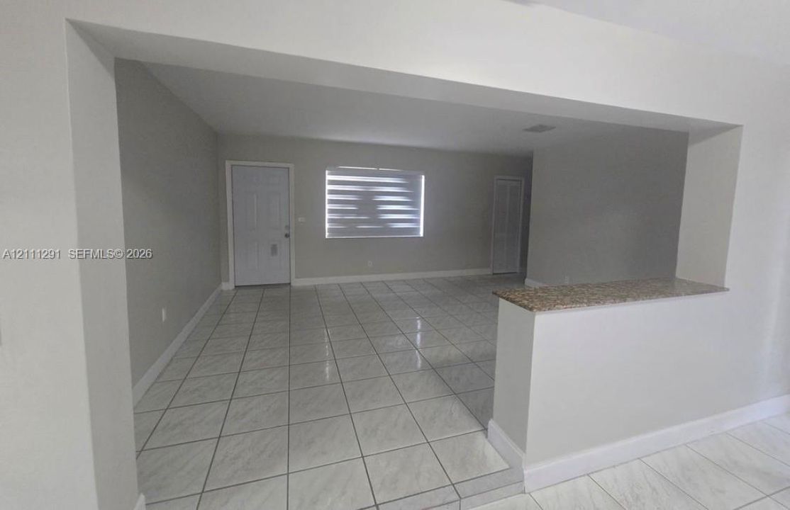 Neutral-toned interior featuring large-format tile flooring, a pass-through counter with a stone-finish top, and tiered window blinds