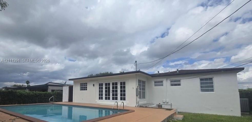 Exterior featuring a white stucco facade, inground swimming pool with metal ladder, concrete pool deck, and multi-pane French doors