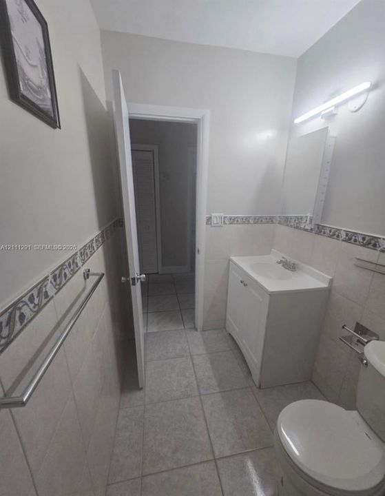 Ceramic tile flooring, vanity cabinet with integrated sink, patterned tile border, wall-mounted light fixture, and metallic towel bar