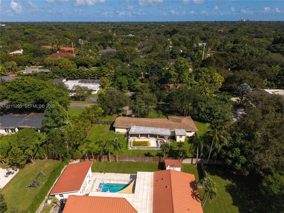 Aerial perspective featuring expansive lots with mature trees, metal roofing, and private swimming pools