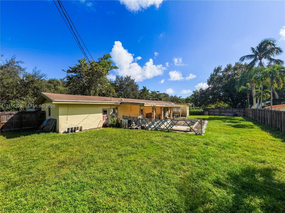 Expansive backyard featuring a large grass lawn, perimeter wood fencing, and mature palm trees