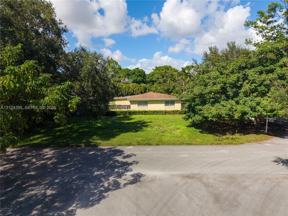 Expansive lot featuring mature trees, manicured lawn, and a light-toned exterior dwelling