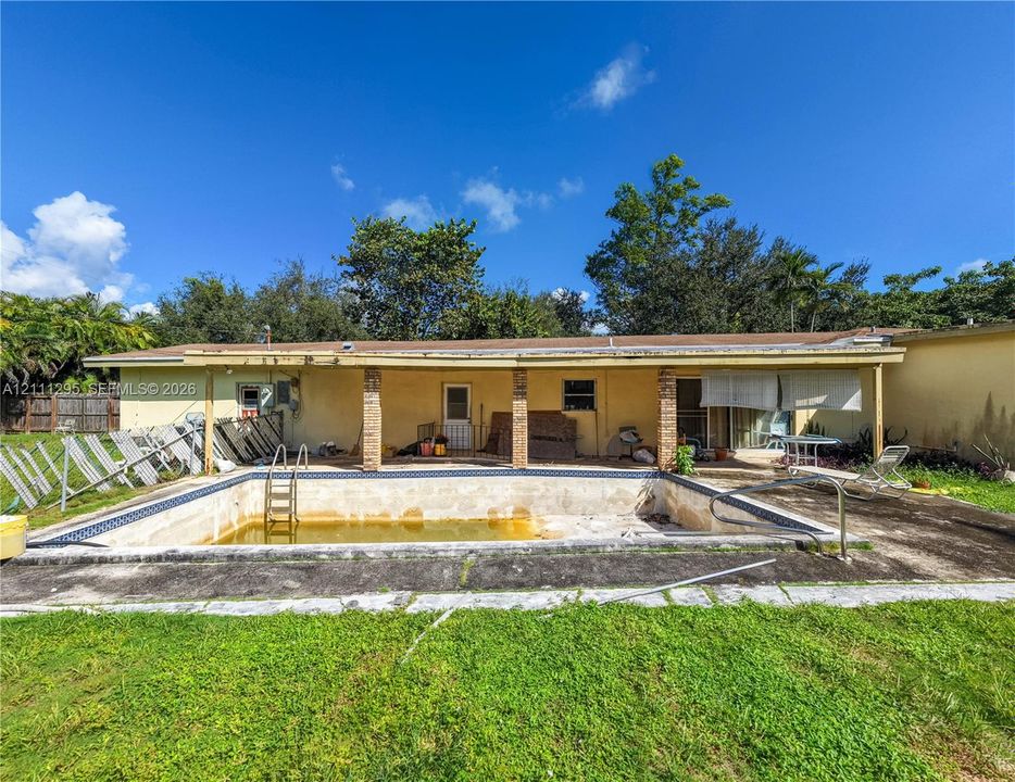 Rear exterior featuring a covered patio, brick support columns, and an in-ground swimming pool