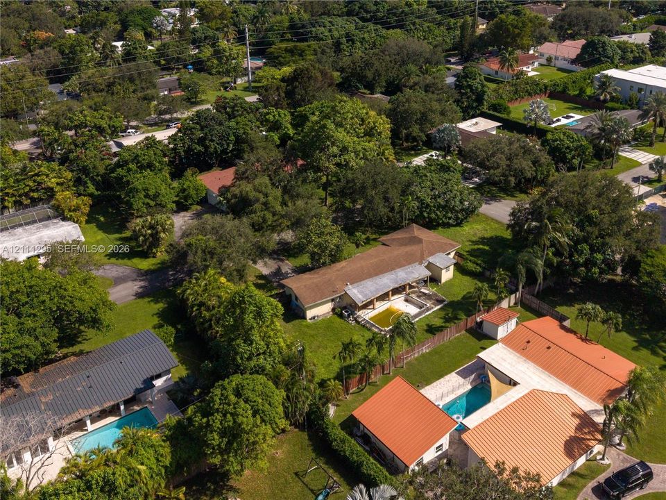 Aerial perspective featuring multiple single-story residential structures, pitched shingle roofing, private swimming pools, and mature tree-lined landscaping