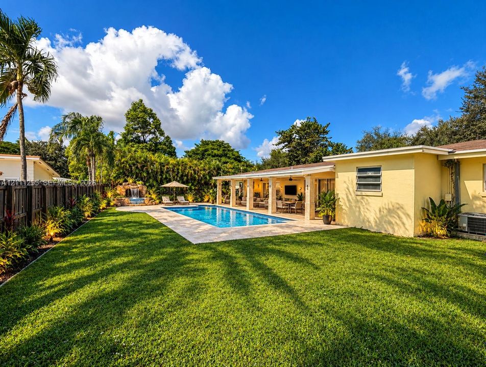 Conceptual rendering - Backyard featuring an in-ground swimming pool with a rock water feature, a covered patio with recessed lighting, and a manicured lawn enclosed by a perimeter fence