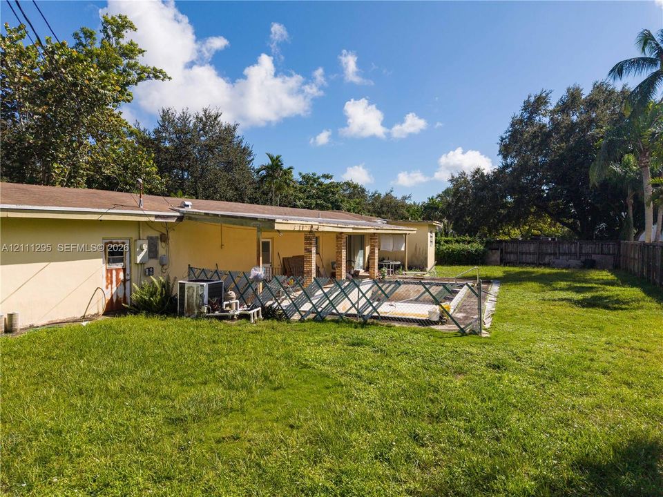 Expansive backyard featuring a large grass lawn, a swimming pool with perimeter fencing, a covered patio area, and mature perimeter trees
