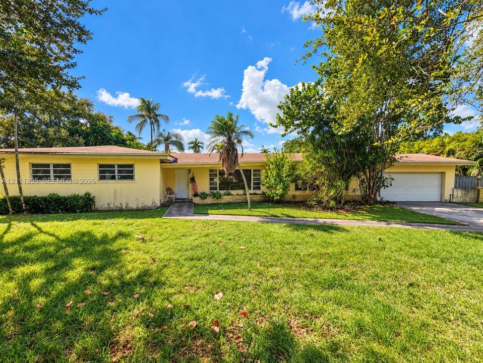 Single-story residence featuring a low-pitched roofline, light-colored exterior finish, attached two-car garage, and expansive front lawn with mature landscaping
