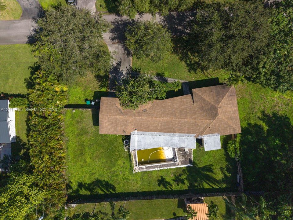 Aerial perspective featuring a shingled roof, concrete pool, and expansive grounds with mature trees